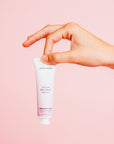 A person holding a tube of Grace & Stella Lavender Body Lotion (473ml) free gift for skin against a pink background.